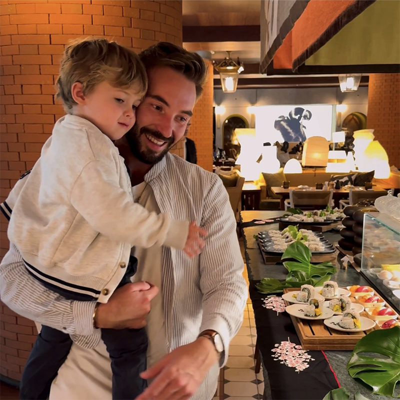 Man holding small boy in a restaurant looking at sushi