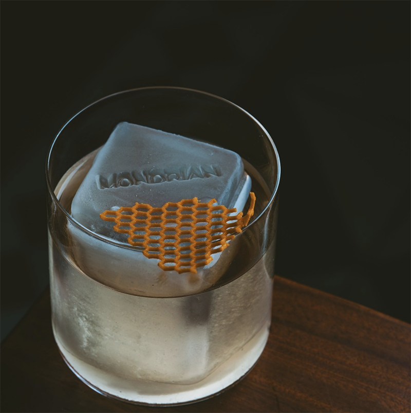 Cocktail in a short glass with large square ice cube and waffle garnish