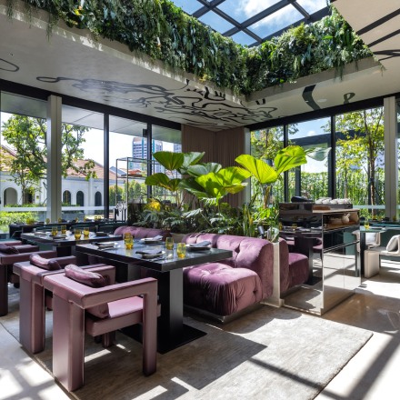 Interior of Bottega di Carna restaurant with plush, purple seating, tables and a skylight with plants