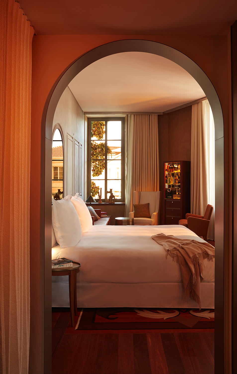 A cozy bedroom with a bed, chair, table, and a window offering a serene view.