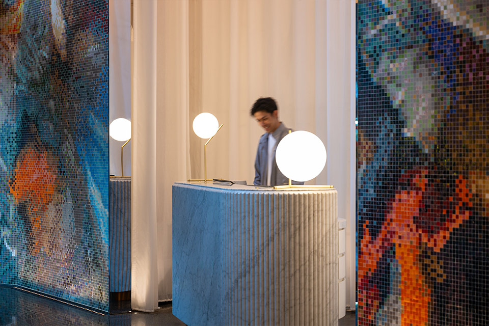 Person at the Mondrian Hong Kong hotel reception with hanging lights and a check-in desk and colorful wall mural