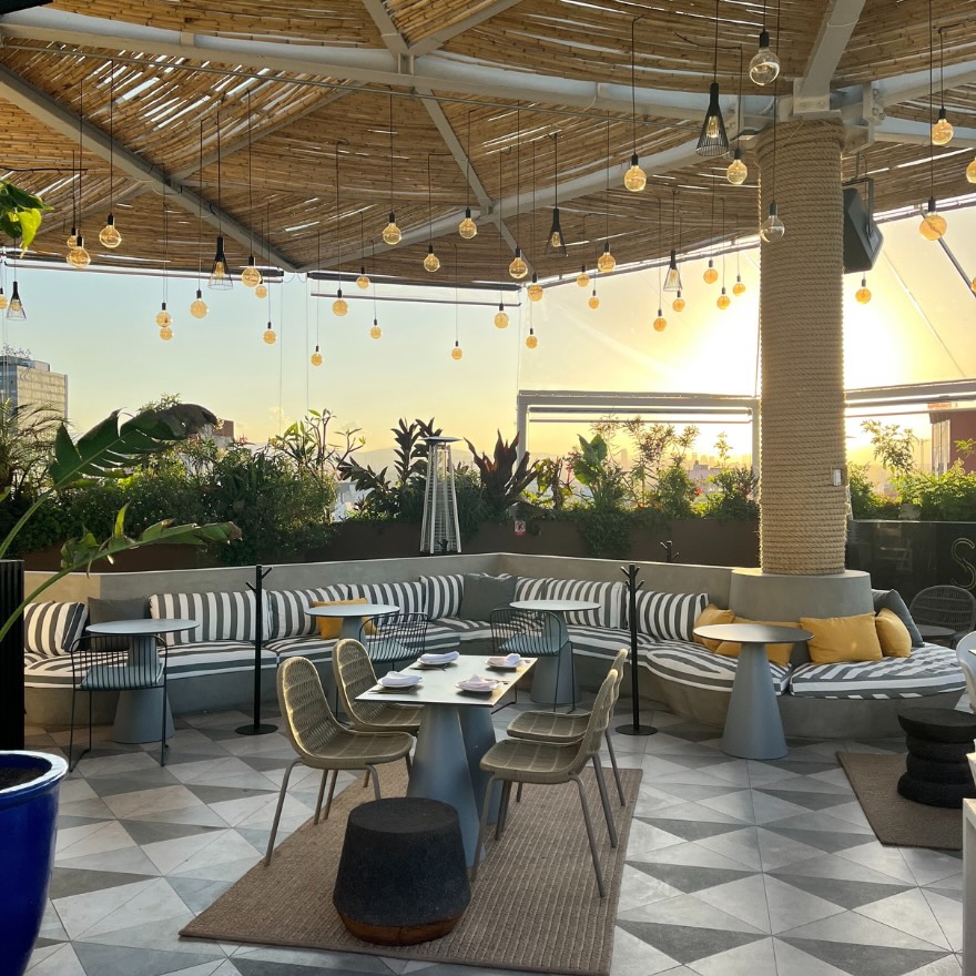 a rooftop terrace with hanging lights and modern furniture at sunset