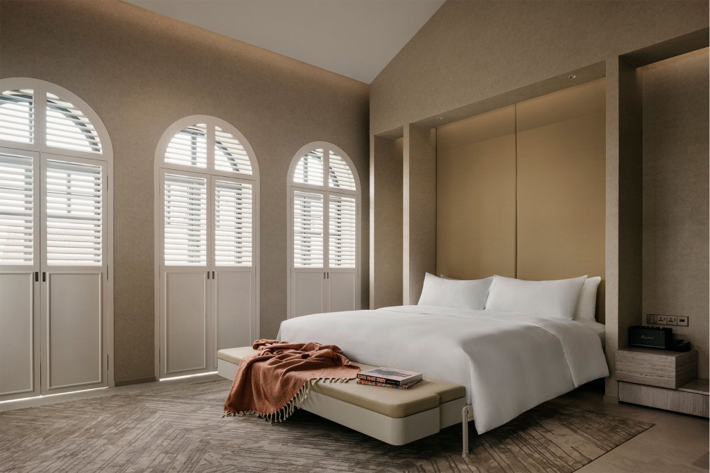 A cozy bedroom with a comfortable bed, a stylish chair, and oversized windows with white shutters.