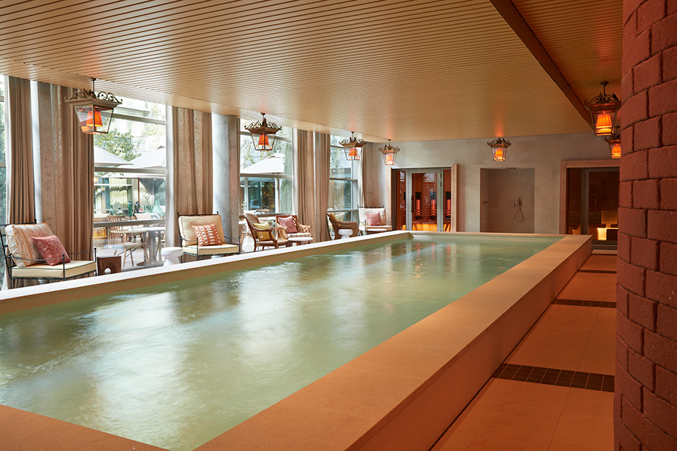 Longue piscine intérieure photographiée de côté avec des chaises longues positionnées d'un côté près des fenêtres