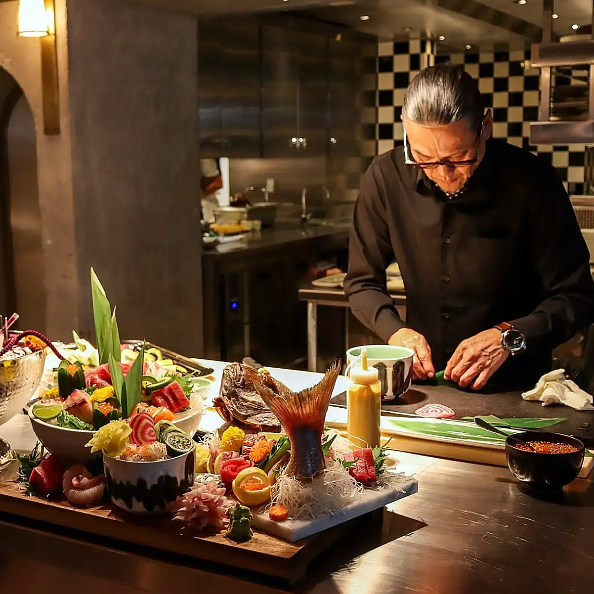 El chef Morimoto cocinando en una mesa con varios platos preparados en primer plano.