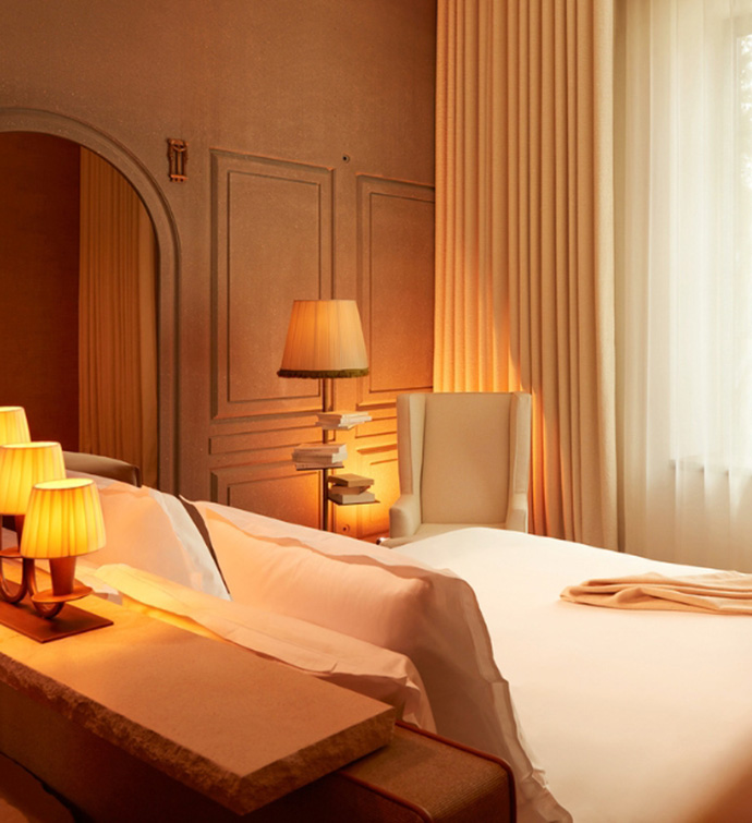 A stone table behind a bed, with an arm chair and floor lamp in the background