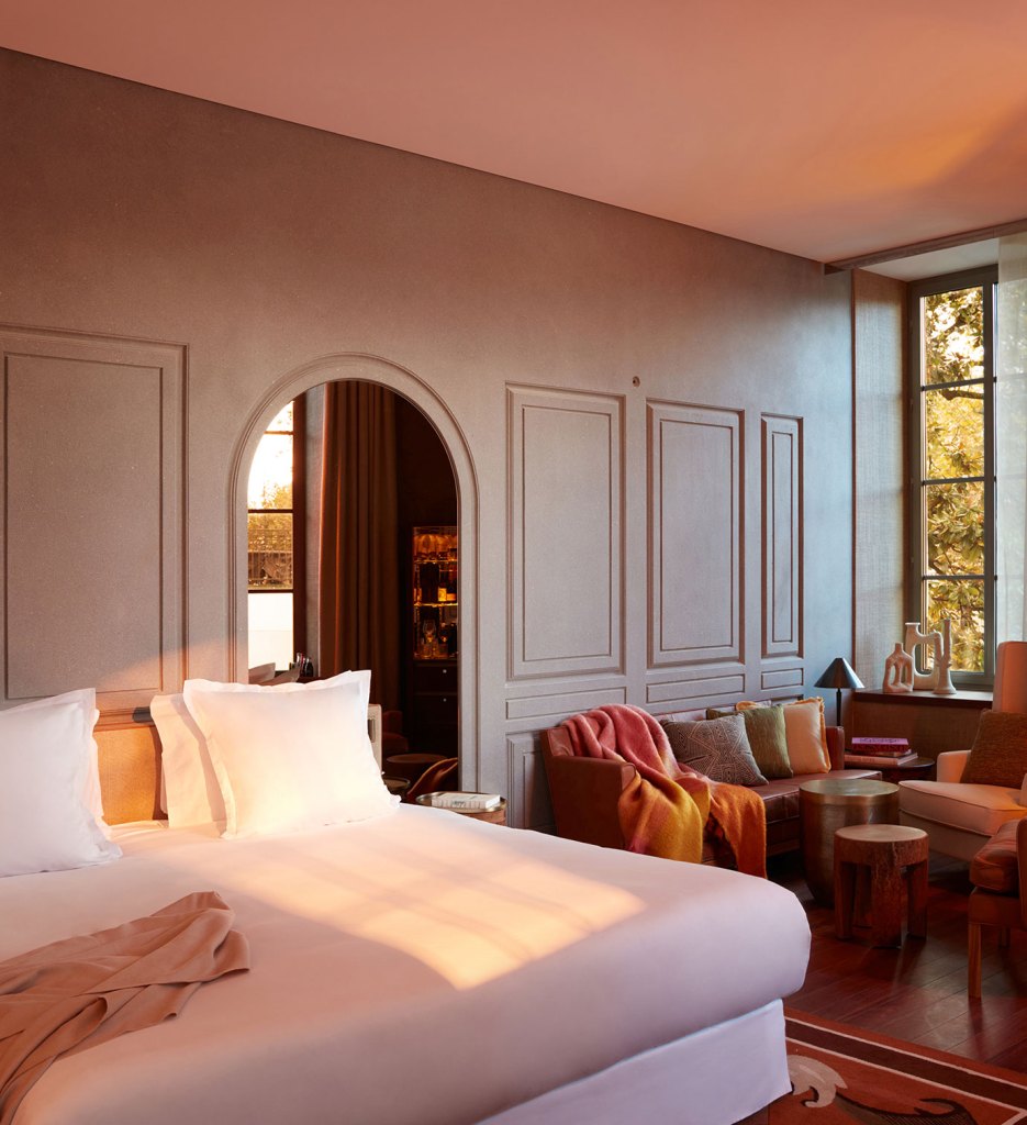 A cozy bedroom with a bed, chair, table, and a window offering a serene view.