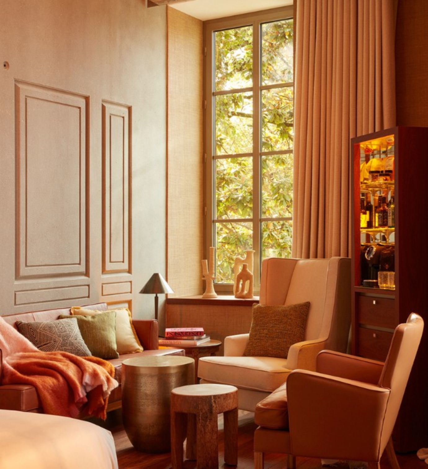 Seating area with a sofa, two armchairs and 2 coffee tables, in front of a tall bar unit, bathed in golden light