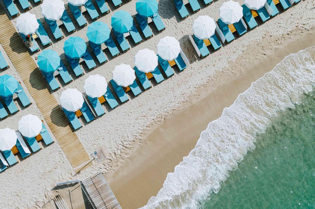 Vue aérienne d'une plage de sable aux eaux turquoise et chaises longues turquoise avec parasols blancs et turquoise