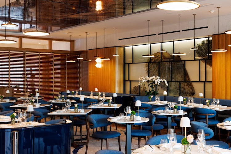 Large dining room with small white round and square tables and blue upholstered dining chairs 