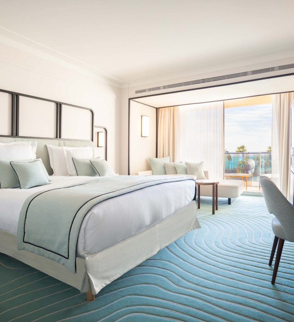 Spacious hotel room with blue carpet and bed.