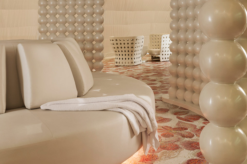 Zona de spa de Mondrian Doha con un sofá circular blanco, suelos florales rojos y blancos y paredes salpicadas de cuentas blancas.