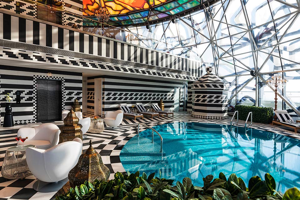 Piscine ronde du spa Mondrian Doha avec un sol et des murs noirs et blancs, ainsi qu'un plafond en vitrail.