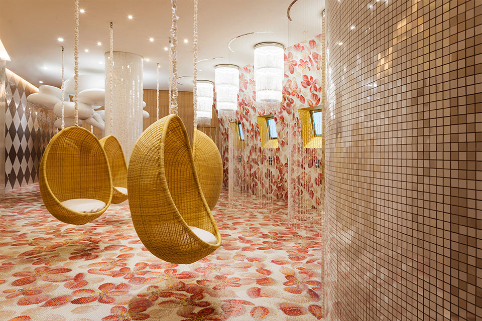 Espace spa Mondrian Doha avec des murs et des sols floraux rouges et blancs, et des chaises cocon en osier suspendues.