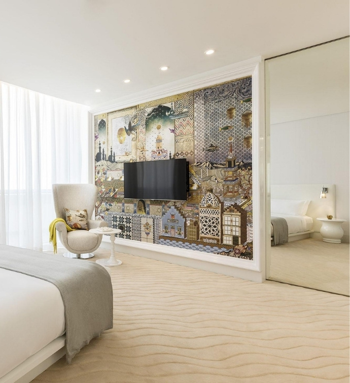 Hotel room with a bed, chair, colorful wall mural, tv and oversized mirror