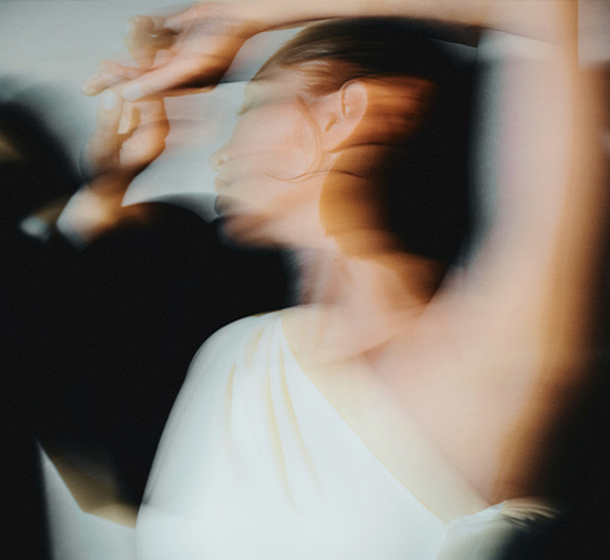 Image floue représentant une femme en robe blanche avec une épaule dénudée en train de danser.