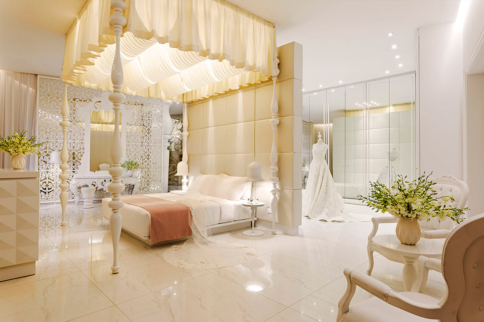 Suite Opal au Mondrian Doha avec un lit King Size à baldaquin blanc, avec une robe de mariée exposée dans une pièce avec des miroirs.