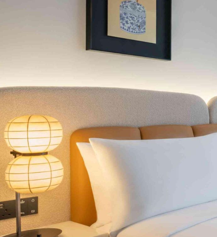 Bed with beige headboard, a lamp on a nightstand and picture on the wall