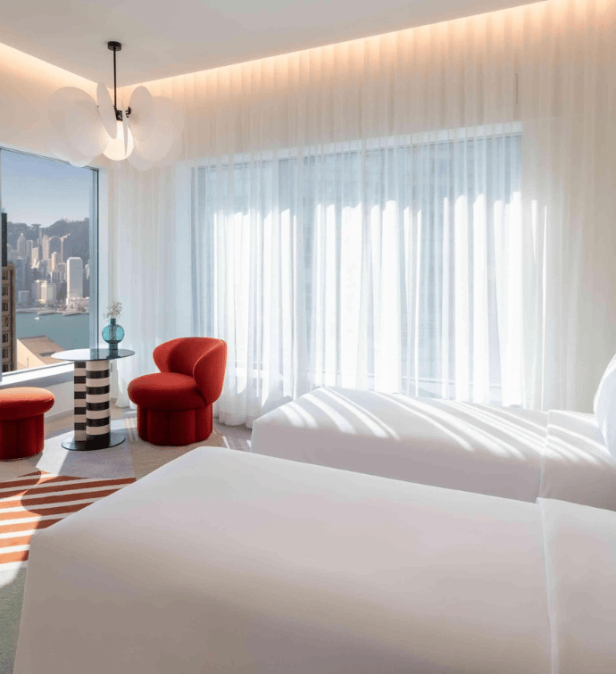 two twin beds in a room with a seating area and floor to ceiling windows that overlook Victoria Harbour