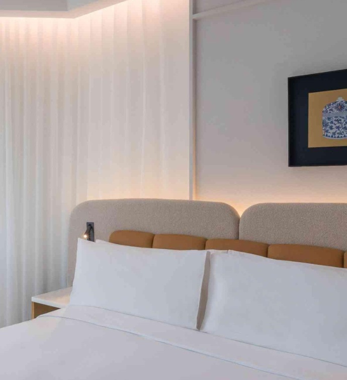 Hotel room with neatly made bed, yellow headboard and curtains drawn