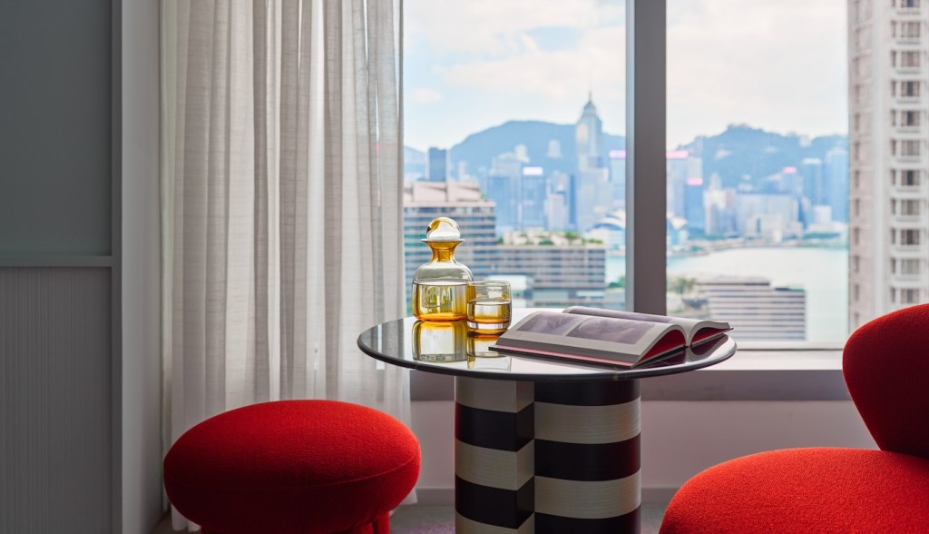 small black and white striped table with glass and book on top and two red chairs nearby and a window looking out to the city