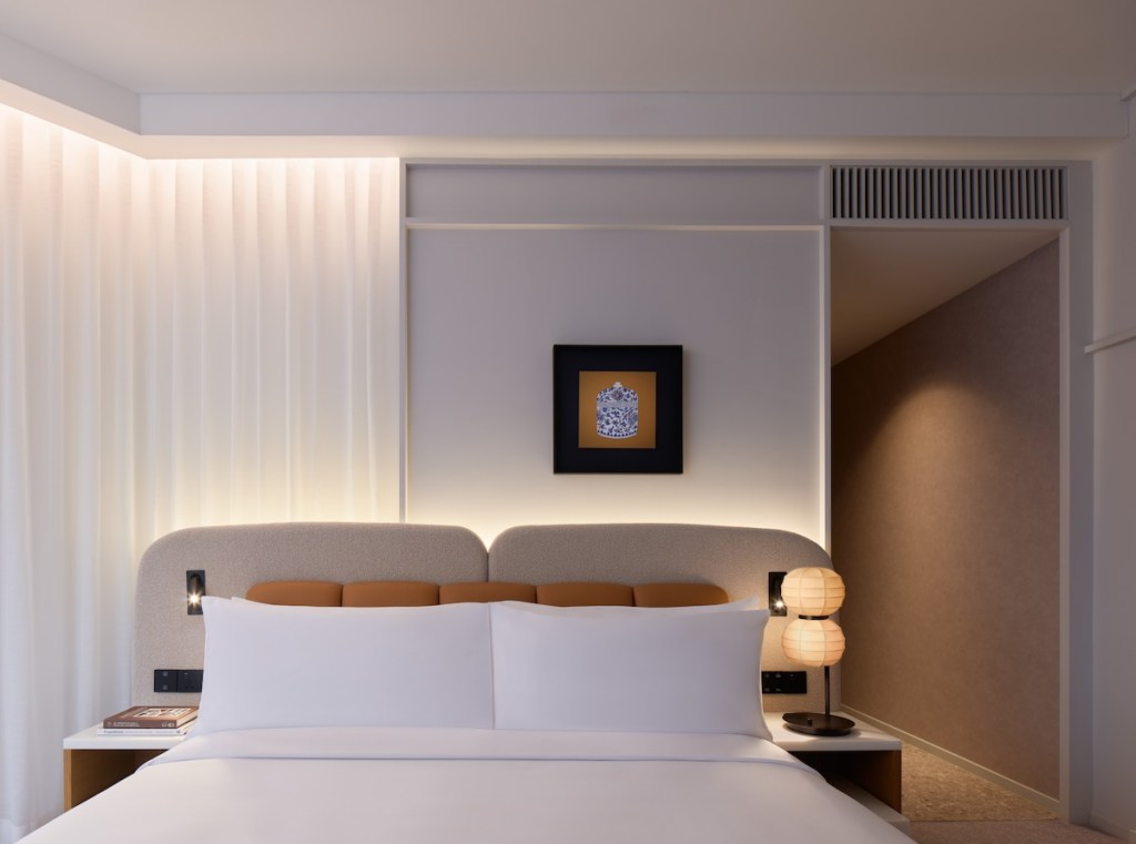 Close up image of white bed with grey and light brown headboard with small framed art hanging overhead