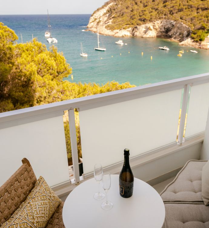 Balcony with small white table ad bottle of champagne with two glasses on it and view of the blue sea in the background