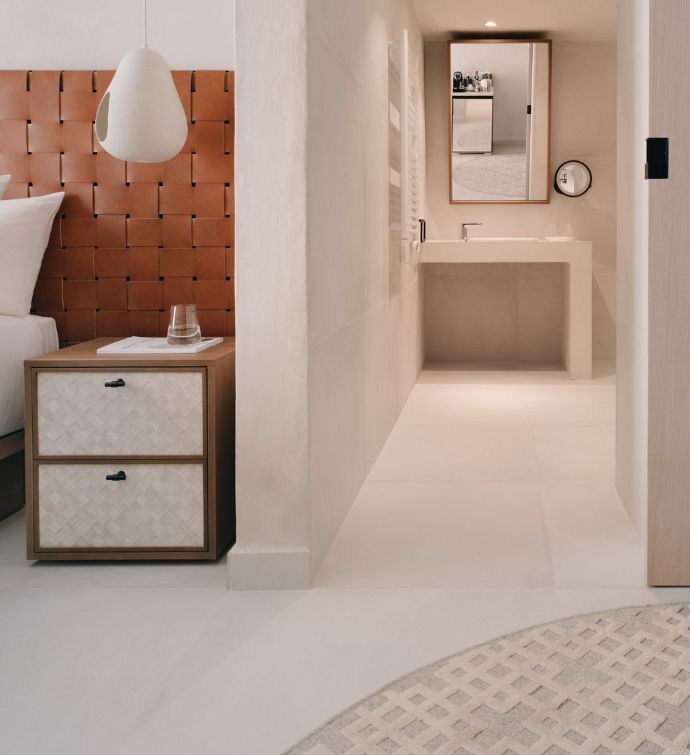 Habitación de hotel con mesita auxiliar, cabecero de color óxido y, al fondo, el lavabo y el espejo del baño