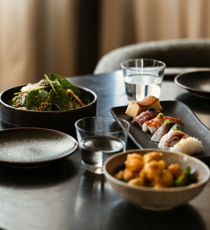 Plate of sushi and other small dishes on a black table with two glasses of water