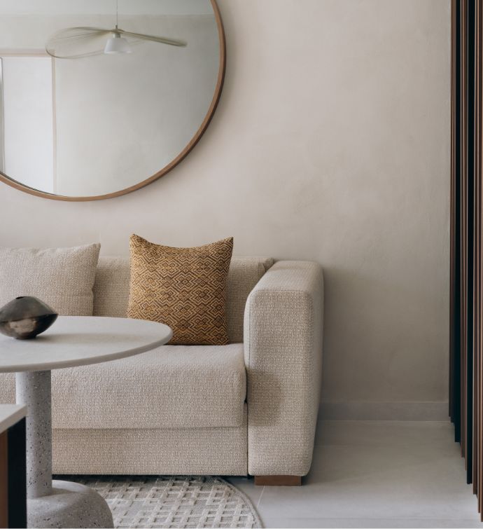 Hotel suite room with cream sofa, small cream round table, and a round framed mirror on a wall behind the sofa