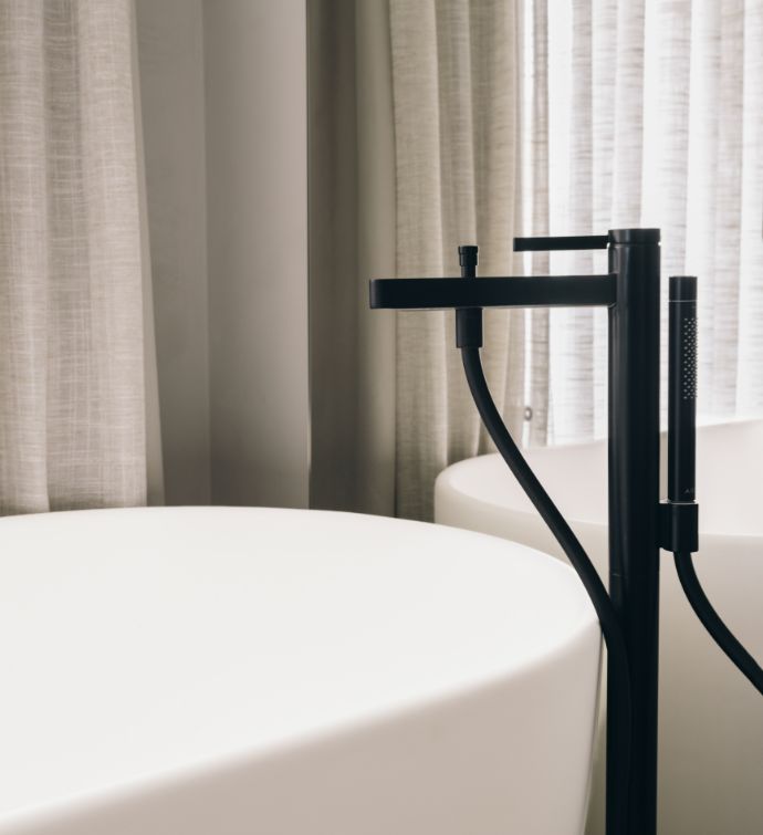 Close up of a white bathtub with black hardware and curtains behind it