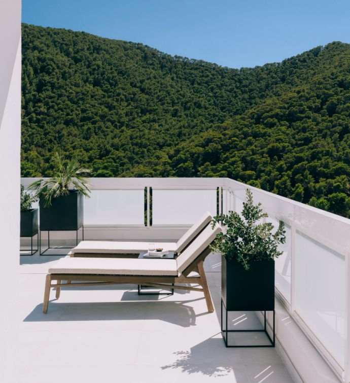 White terrace with two cushioned lounge chairs and green mountains in the background