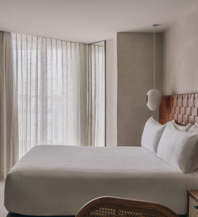 Una cama bien hecha, con sábanas blancas, un cabecero de cuero y cortinas en las ventanas