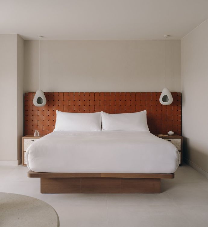 Large white bed with chestnut brown weaved headboard and white hanging lights on either side of the bed