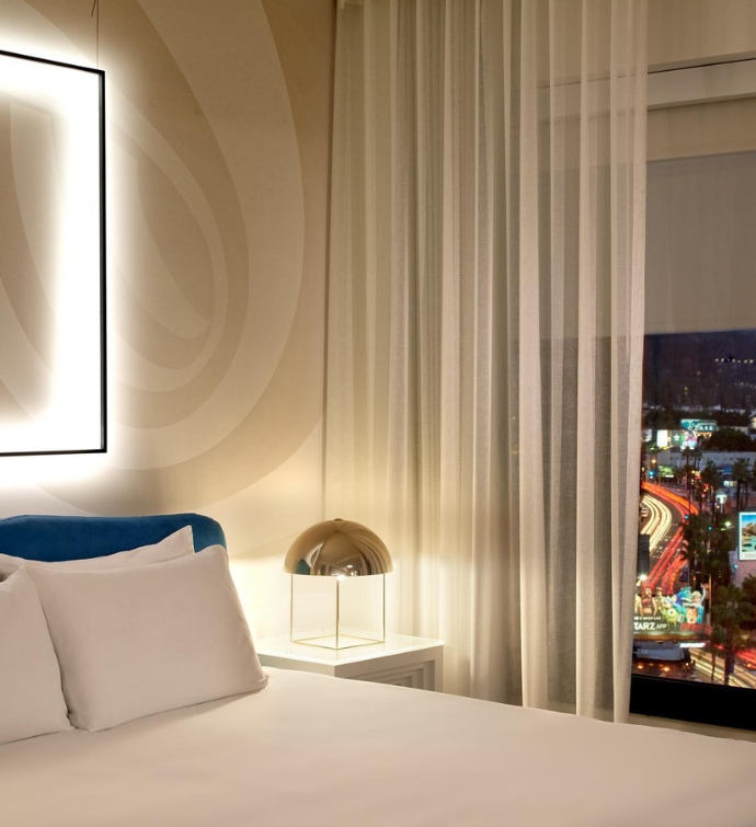 Night image of a bed with nightstand and light overlooking Los Angeles