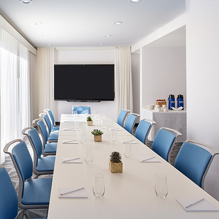 Large, white boardroom with a long table, blue chairs and TV.