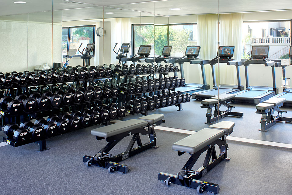 Gimnasio con un gran espejo en la pared, mancuernas, cintas de correr y bancos para levantar pesas.