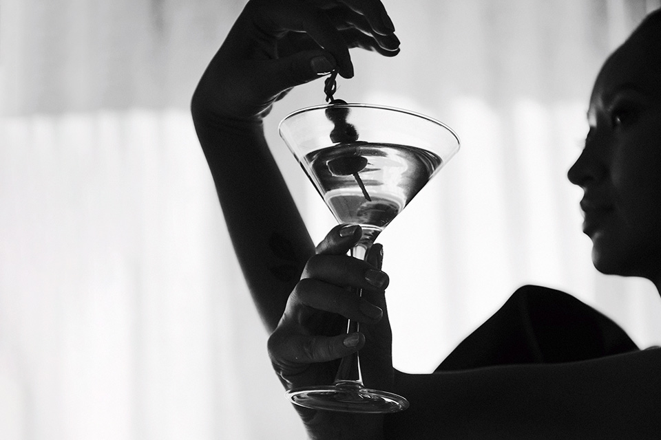 Fotografía en blanco y negro de una mujer sosteniendo una copa de martini con tres aceitunas.