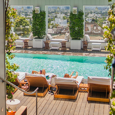 Skybar LA pool on the rooftop of Mondrian Los Angeles, with two people laying in daybeds looking at the city views.