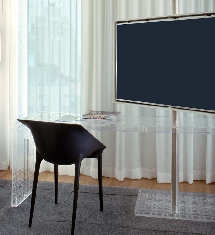 Televisor grande con una mesa transparente y una silla negra de plástico