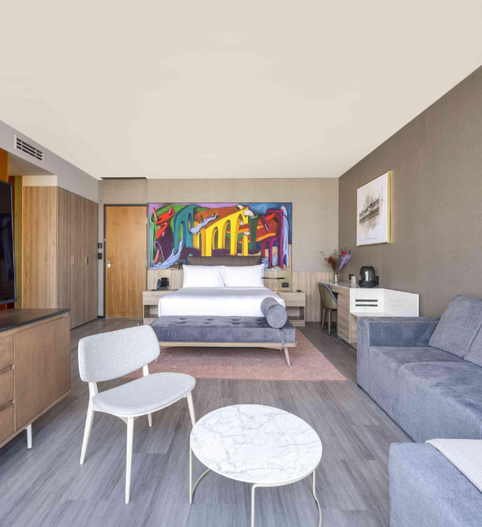 a large bedroom with bright modern art behind the bed, and a sitting area with a couch and mounted hdtv