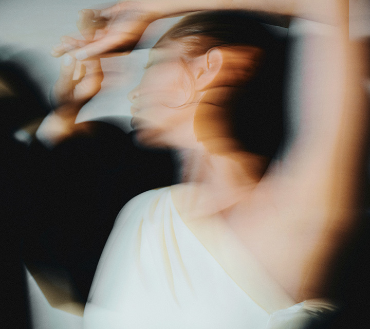 Image floue représentant une femme en robe blanche avec une épaule dénudée en train de danser.