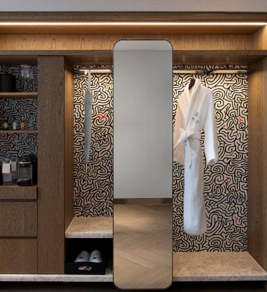 Wooden wardrobe with black and white patterned backsplash with floor-length mirror, white robe hanging, and a grey umbrella