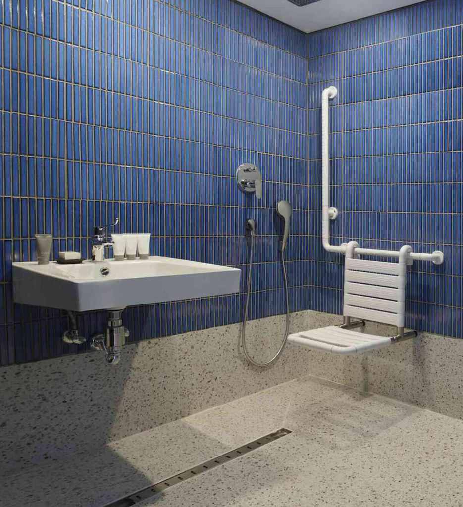 Large blue tiled bathroom with accessible shower, toilet, and sink