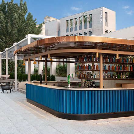 Outdoor bar with blue details and a brass roof overhead with cream modern building in the background.