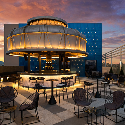 Outdoor lounge space with small black outdoor chairs and bistro tables with a circular, modern bar with domed roof in the background.