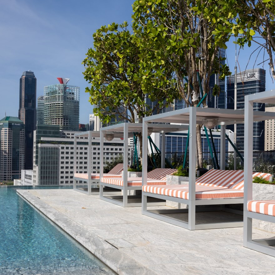 A series of poolside cabanas with white and orange striped daybeds on the rooftop of Mondrian Singapore Duxton.