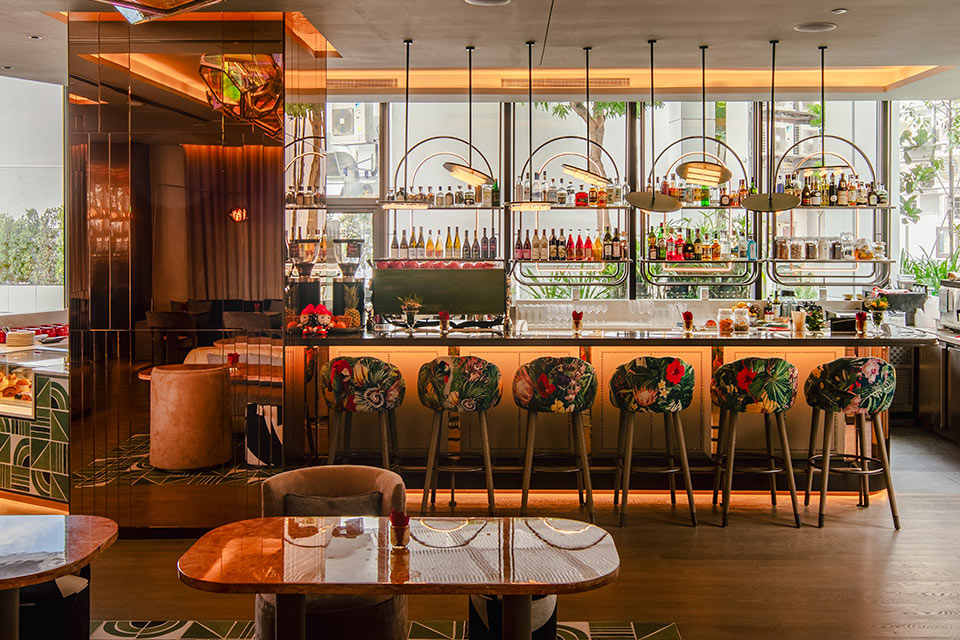 Warmly lit bar with modern pendant lights, floral patterned barstools, and gold lighting accents throughout. 