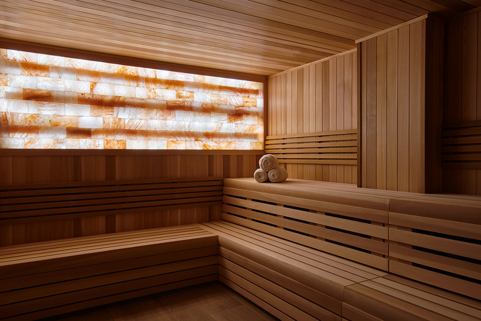 Sauna de madera relajante con piedras de sal en la pared y toallas de spa enrolladas.