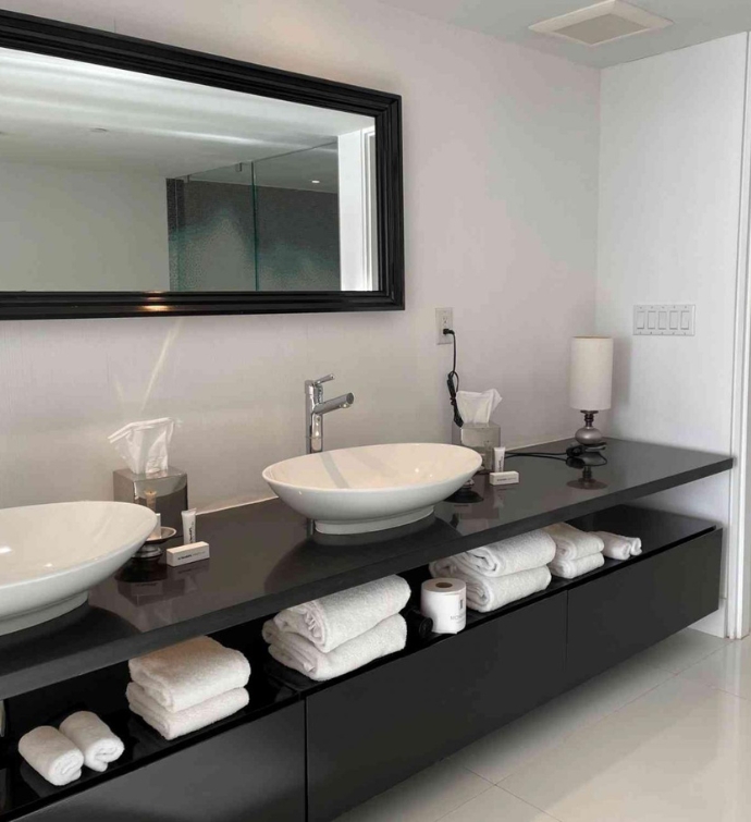 Double bathroom sinks and large black framed rectangular mirror with towels folded under the sink